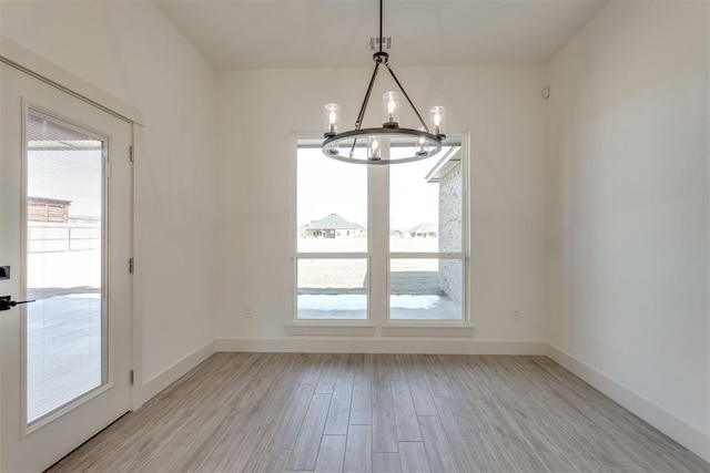 unfurnished dining area featuring a healthy amount of sunlight, a notable chandelier, and light hardwood / wood-style floors