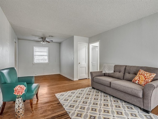 living room with ceiling fan, a textured ceiling, and light wood-type flooring