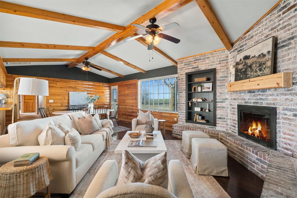 living room featuring built in shelves, lofted ceiling with beams, a brick fireplace, ceiling fan, and hardwood / wood-style floors