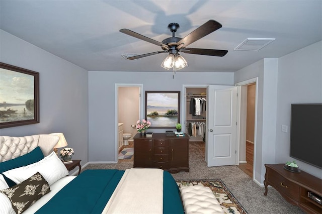 bedroom featuring ensuite bathroom, a walk in closet, light colored carpet, ceiling fan, and a closet