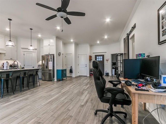 office area featuring sink, a barn door, ceiling fan, and light wood-type flooring