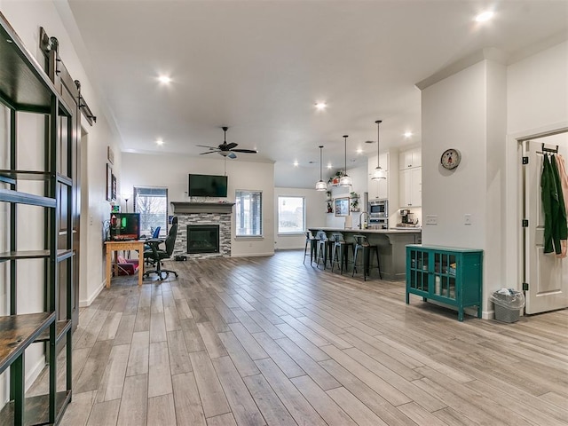 living room featuring ceiling fan, a barn door, a stone fireplace, and light wood-type flooring