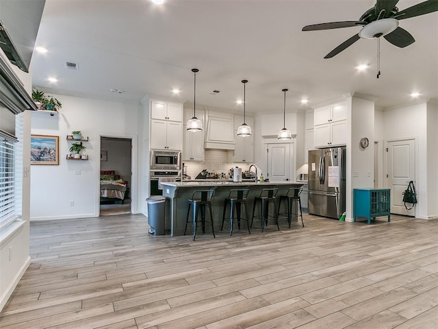 kitchen with stainless steel appliances, decorative light fixtures, an island with sink, and white cabinets