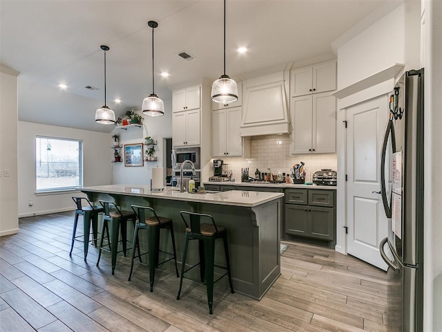 kitchen with white cabinetry, decorative light fixtures, stainless steel appliances, and an island with sink