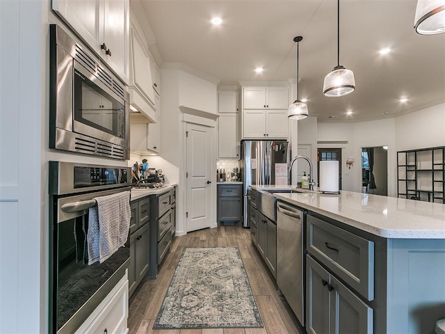 kitchen with pendant lighting, white cabinetry, stainless steel appliances, light stone countertops, and an island with sink