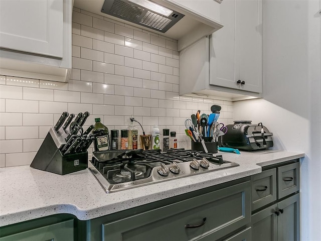 kitchen featuring wall chimney exhaust hood, stainless steel gas cooktop, tasteful backsplash, green cabinetry, and white cabinets