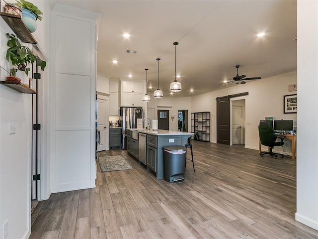 kitchen featuring pendant lighting, white cabinetry, an island with sink, a breakfast bar area, and a barn door