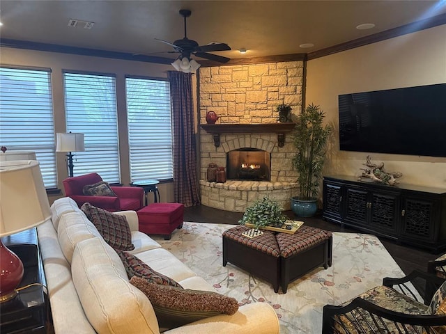 living room featuring crown molding, a stone fireplace, and ceiling fan