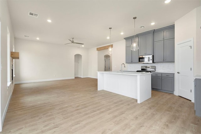 kitchen with hanging light fixtures, appliances with stainless steel finishes, gray cabinets, ceiling fan, and a kitchen island with sink