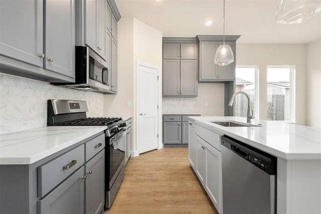 kitchen featuring pendant lighting, sink, light hardwood / wood-style flooring, appliances with stainless steel finishes, and gray cabinetry