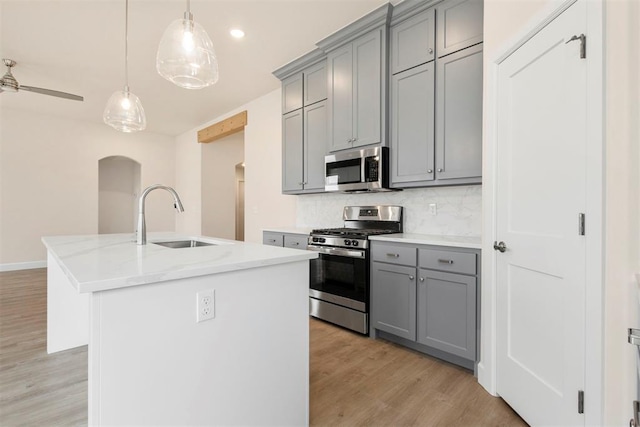 kitchen featuring sink, light stone counters, tasteful backsplash, a center island with sink, and stainless steel appliances