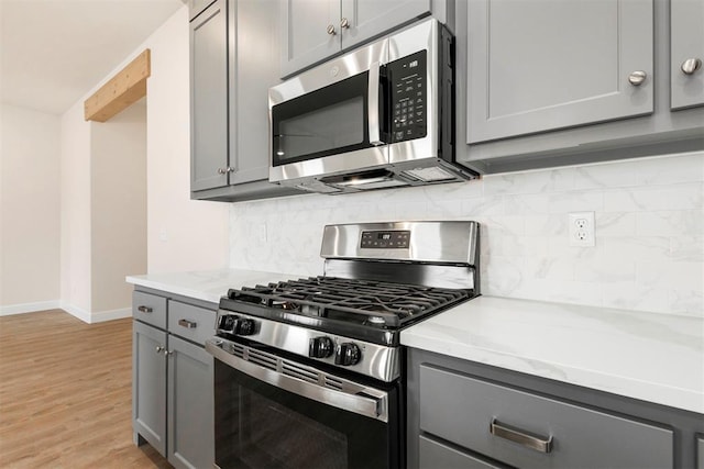 kitchen featuring stainless steel appliances, gray cabinets, light hardwood / wood-style flooring, and backsplash