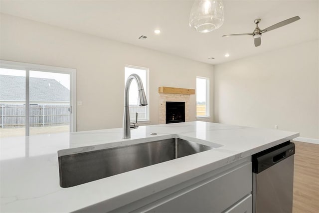 kitchen featuring pendant lighting, sink, stainless steel dishwasher, light stone countertops, and light wood-type flooring