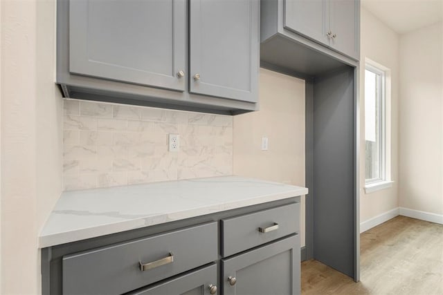 kitchen featuring gray cabinetry, backsplash, and light stone countertops