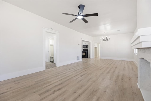 unfurnished living room with ceiling fan with notable chandelier, a fireplace, and light hardwood / wood-style flooring