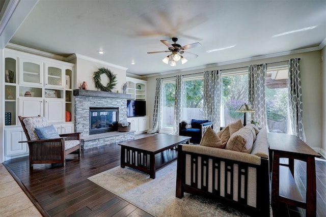 living room with dark wood-type flooring, built in shelves, a stone fireplace, ornamental molding, and ceiling fan