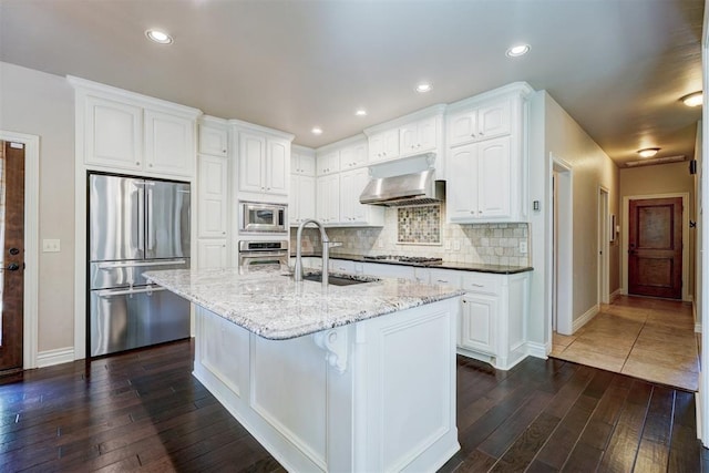 kitchen with sink, white cabinetry, range hood, stainless steel appliances, and light stone countertops