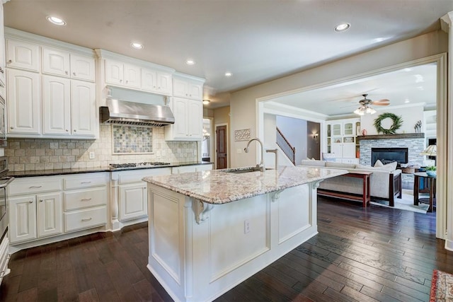 kitchen featuring range hood, stainless steel gas stovetop, sink, dark stone countertops, and dark hardwood / wood-style flooring