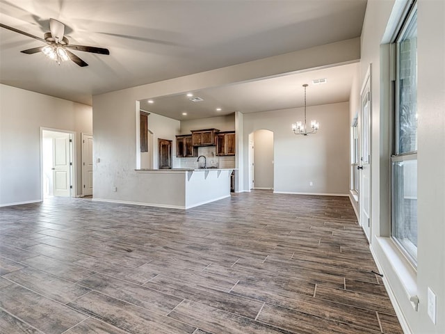 unfurnished living room featuring dark wood-type flooring, ceiling fan with notable chandelier, and sink