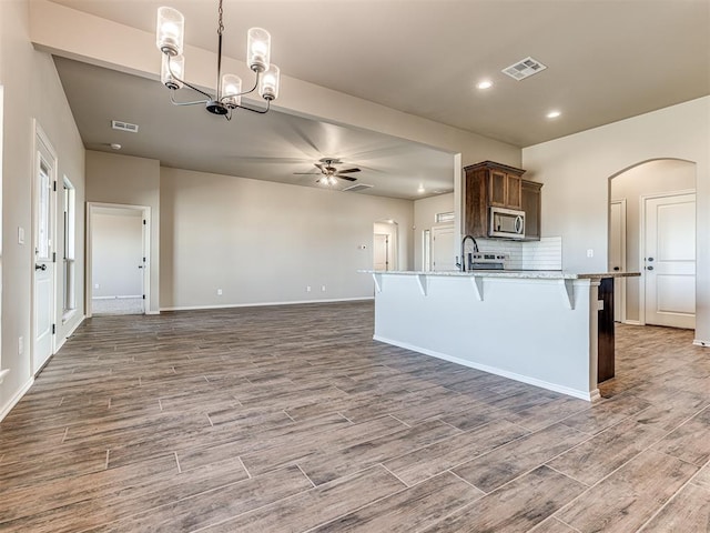 kitchen with a kitchen bar, tasteful backsplash, hanging light fixtures, light wood-type flooring, and ceiling fan with notable chandelier