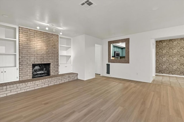 unfurnished living room featuring a brick fireplace, light hardwood / wood-style flooring, and built in features