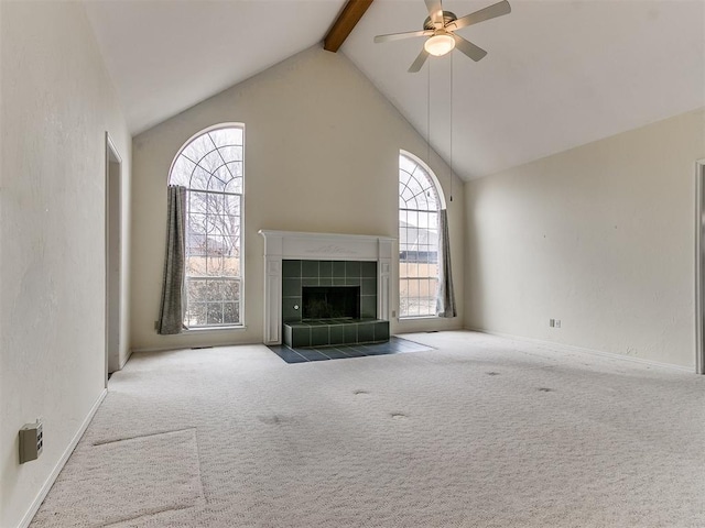 unfurnished living room with high vaulted ceiling, beamed ceiling, carpet flooring, a tiled fireplace, and ceiling fan