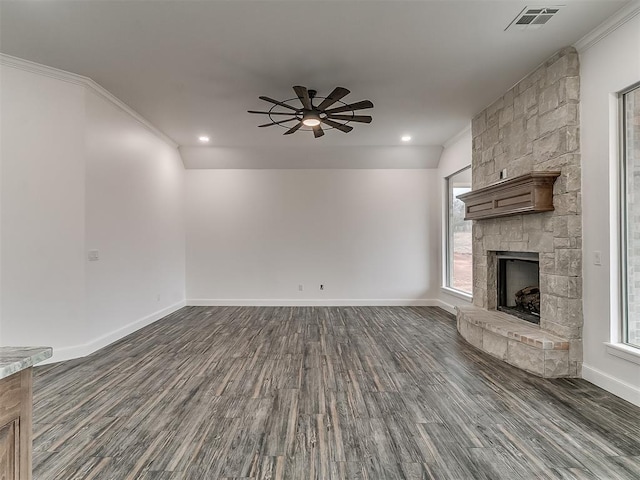 unfurnished living room with crown molding, a stone fireplace, dark hardwood / wood-style floors, and ceiling fan