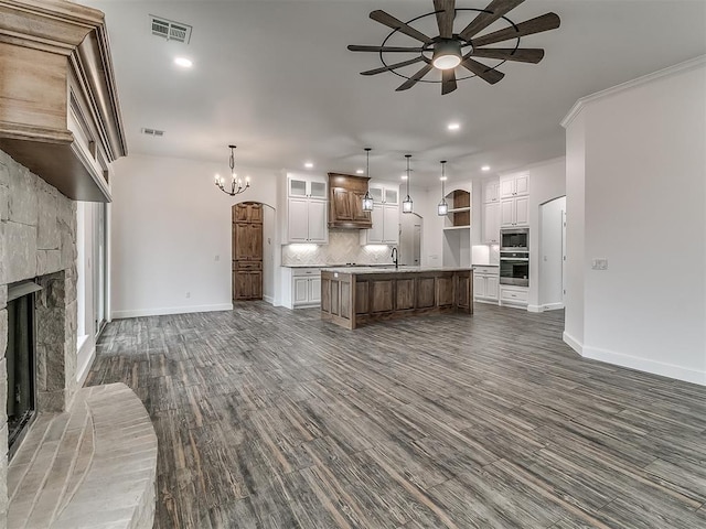 unfurnished living room featuring dark wood-type flooring, a fireplace, ceiling fan with notable chandelier, and sink