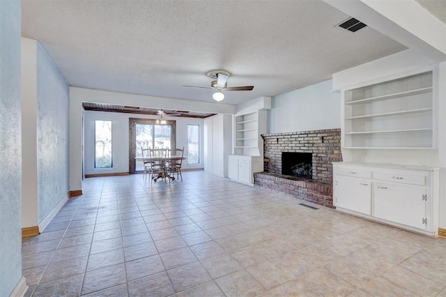 unfurnished living room featuring built in shelves, a brick fireplace, a textured ceiling, light tile patterned floors, and ceiling fan