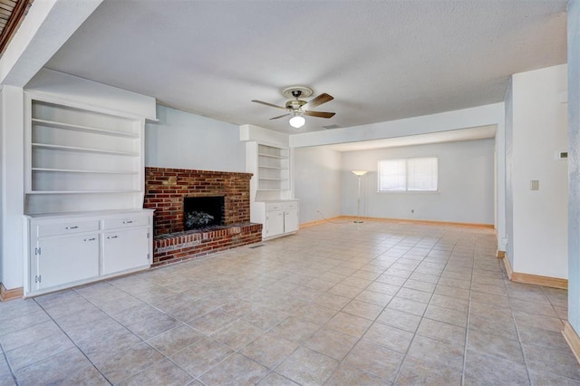 unfurnished living room with built in features, ceiling fan, a textured ceiling, light tile patterned flooring, and a brick fireplace