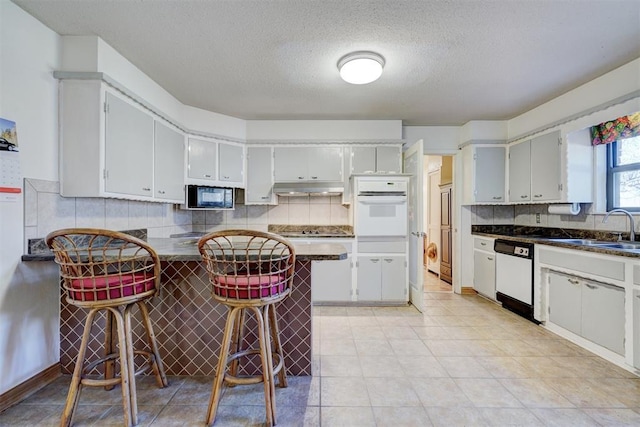 kitchen with white cabinetry, sink, backsplash, a kitchen breakfast bar, and black appliances