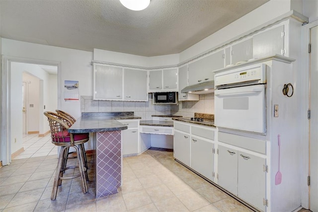 kitchen featuring white cabinetry, backsplash, a kitchen bar, and black appliances