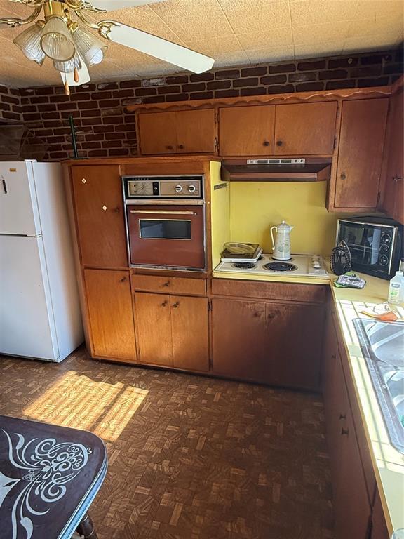 kitchen with white appliances, dark parquet flooring, ceiling fan, and brick wall