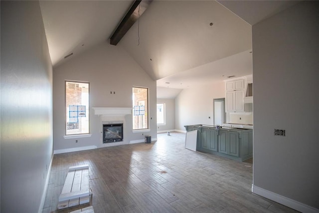 8116 NW 152nd Ter, Edmond, OK 73013 - unfurnished living room featuring beam ceiling, wood finished floors, high vaulted ceiling, and a glass covered fireplace
