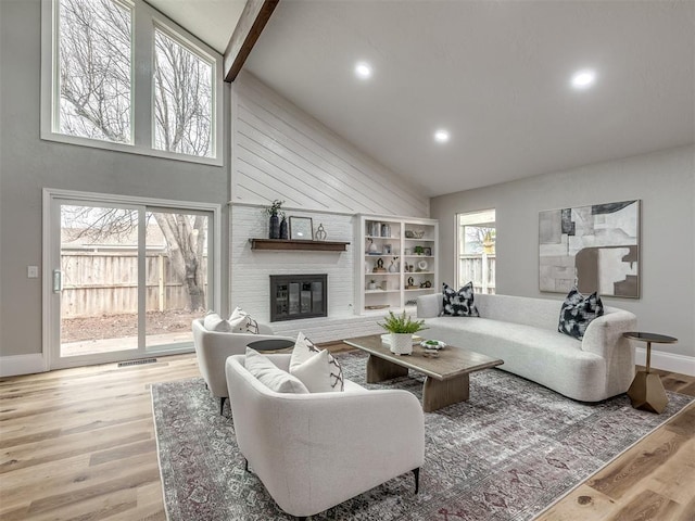 living room with a large fireplace, high vaulted ceiling, and light hardwood / wood-style floors