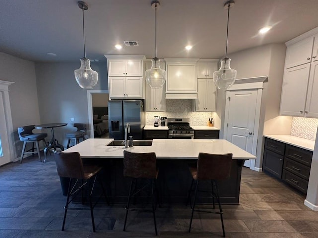 kitchen with an island with sink, stainless steel range with gas stovetop, refrigerator with ice dispenser, and decorative light fixtures