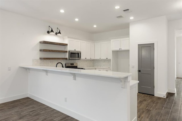 kitchen featuring a kitchen breakfast bar, kitchen peninsula, white cabinets, and appliances with stainless steel finishes