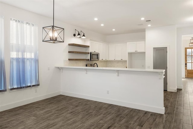 kitchen with pendant lighting, dark wood-type flooring, a breakfast bar, white cabinets, and kitchen peninsula