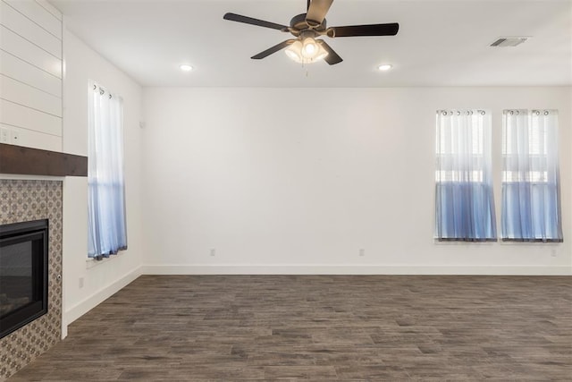 unfurnished living room featuring a tile fireplace, dark hardwood / wood-style floors, and ceiling fan