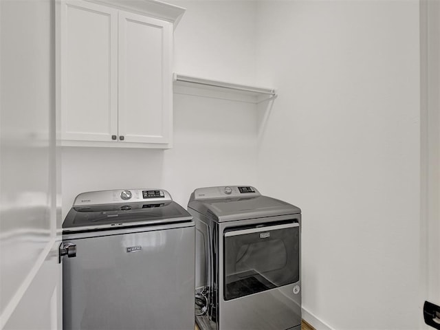 clothes washing area with separate washer and dryer and cabinets