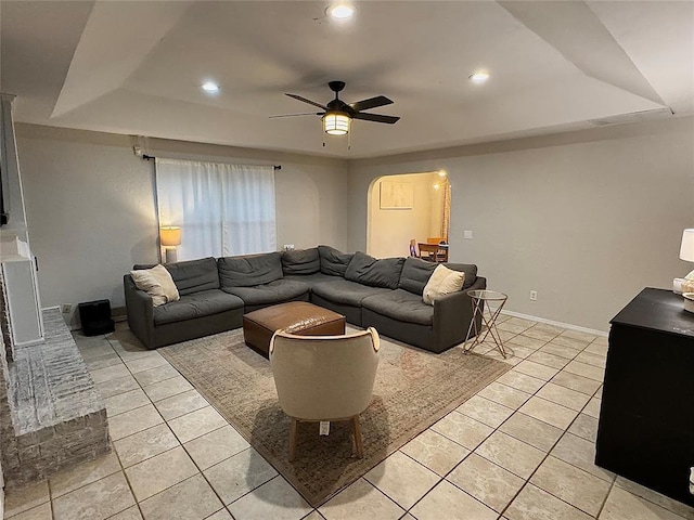 living room featuring light tile patterned flooring, ceiling fan, and a tray ceiling