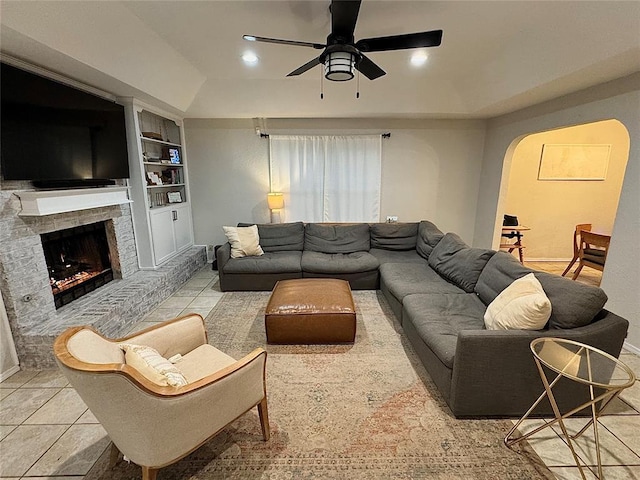 tiled living room with built in shelves, ceiling fan, and a brick fireplace