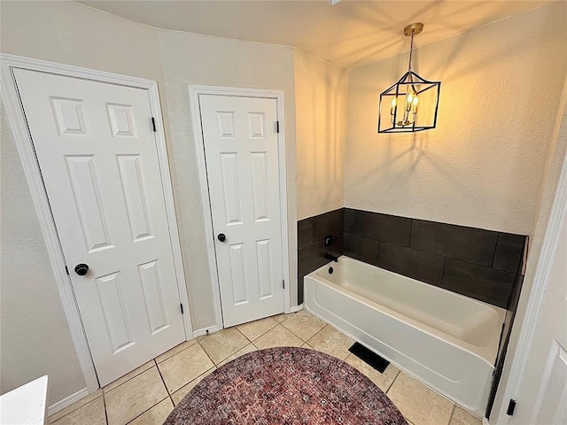 bathroom with an inviting chandelier, a tub to relax in, and tile patterned flooring