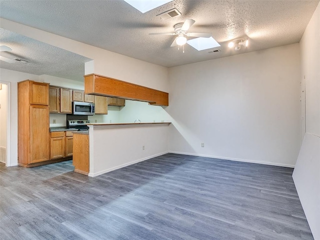 kitchen with appliances with stainless steel finishes, a skylight, dark hardwood / wood-style flooring, ceiling fan, and kitchen peninsula