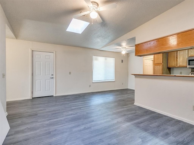 unfurnished living room featuring dark hardwood / wood-style floors, ceiling fan, lofted ceiling with skylight, and a textured ceiling