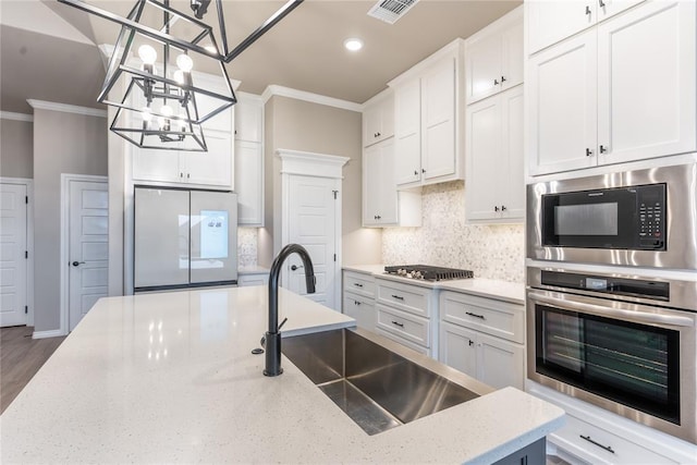 kitchen with appliances with stainless steel finishes, white cabinetry, sink, light stone counters, and crown molding