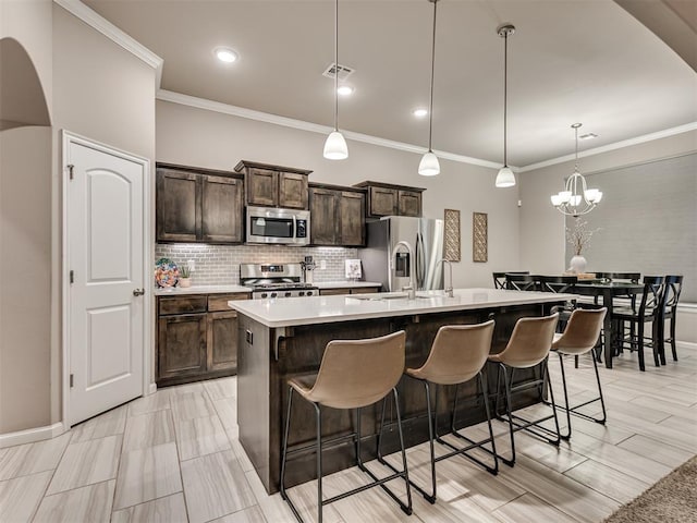 kitchen featuring dark brown cabinets, appliances with stainless steel finishes, hanging light fixtures, and a center island with sink