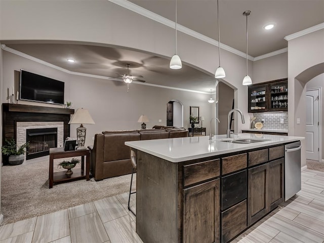 kitchen featuring pendant lighting, a fireplace, sink, dark brown cabinets, and a center island with sink