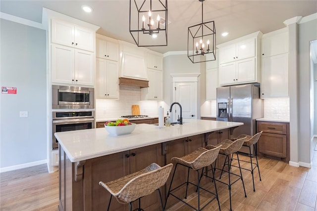 kitchen with stainless steel appliances, an island with sink, sink, and white cabinets