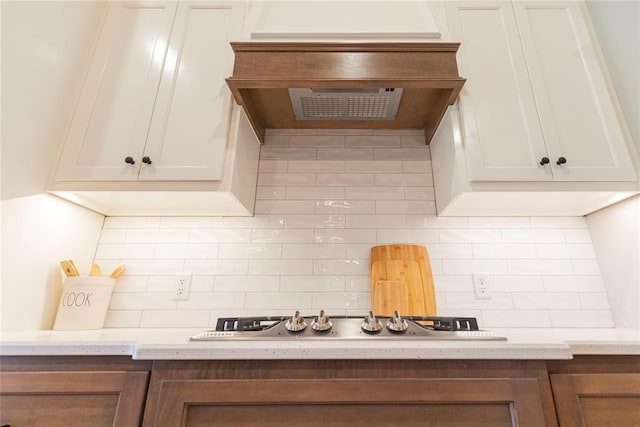 kitchen with premium range hood, stainless steel gas stovetop, light stone counters, and backsplash